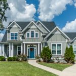 A two-story gray house with a blue front door, white trim, white windows, and an asphalt shingle roof.