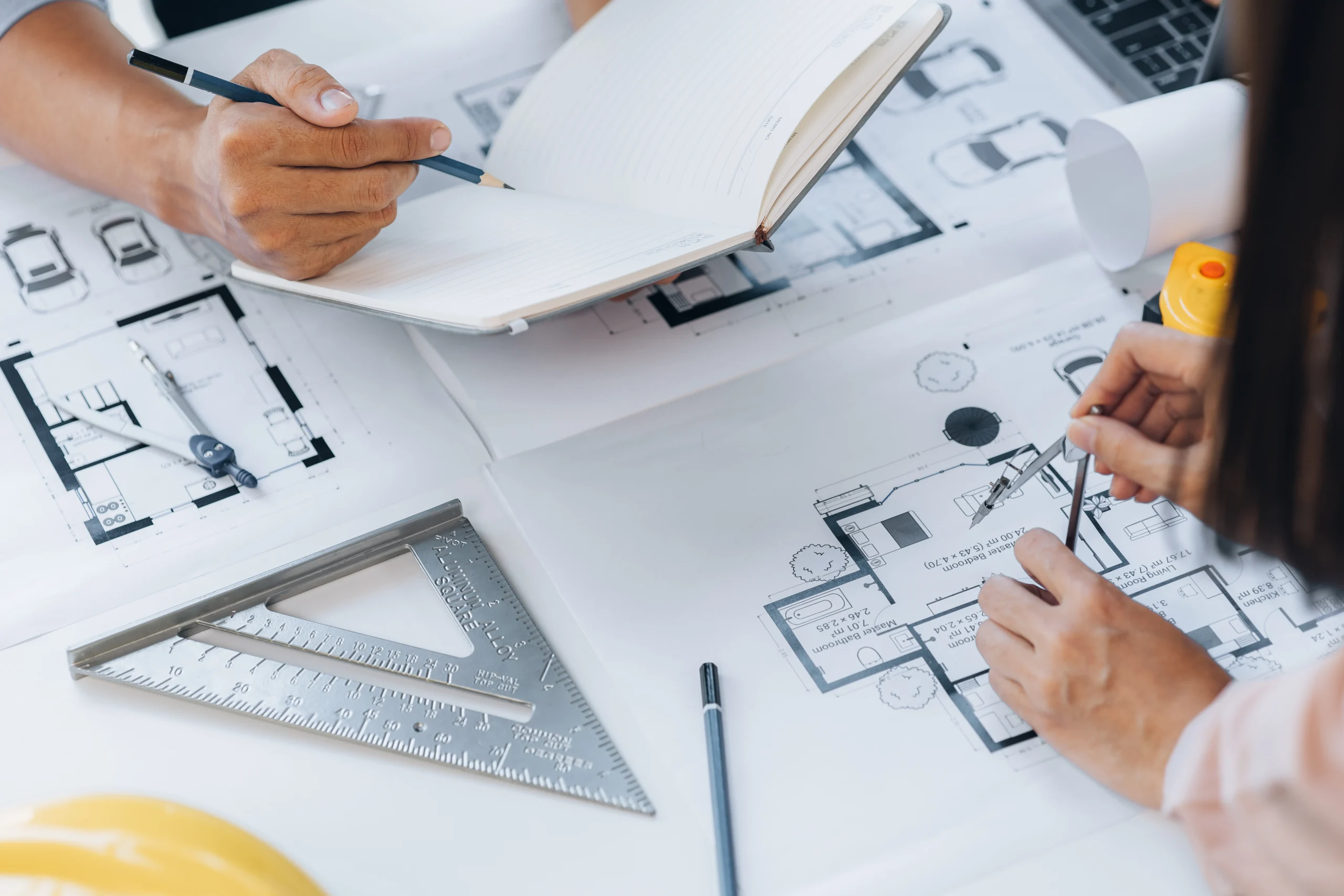 Spacious Custom Home Design In Defiance, MO | BECC Builders, LLC Two architects working on the floor plans of a house with a protractor and a notebook.