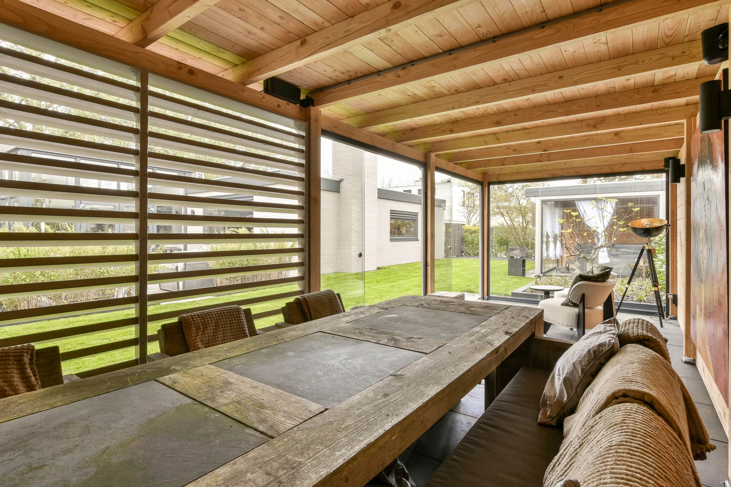 A back patio with a wooden roof, wooden walls, windows, and a wooden table with chairs.